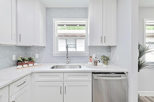 kitchen featuring tasteful backsplash, stainless steel dishwasher, white cabinets, light stone counters, and sink