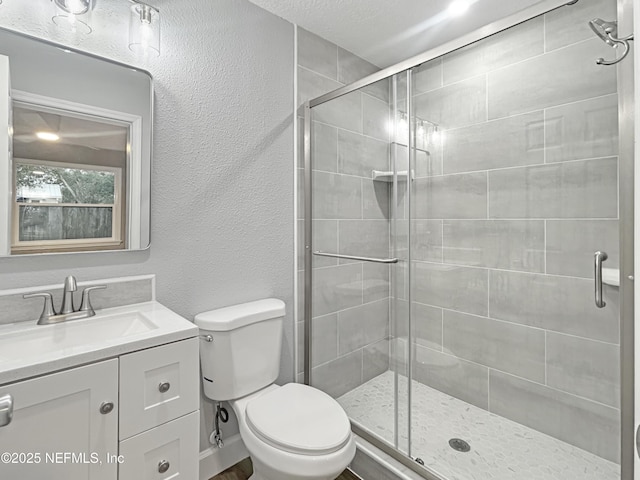 bathroom featuring toilet, vanity, a shower with door, and a textured ceiling