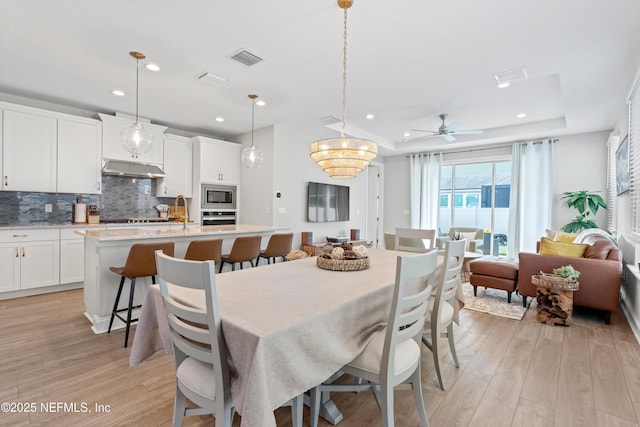 dining area with ceiling fan, a tray ceiling, sink, and light hardwood / wood-style flooring