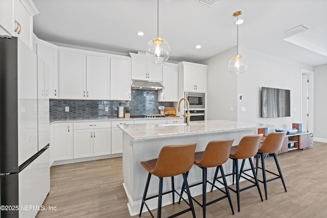 kitchen featuring pendant lighting, stainless steel appliances, an island with sink, and white cabinets