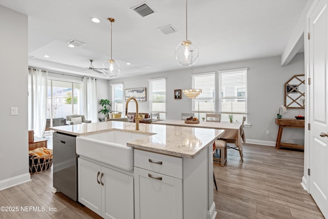 kitchen with a kitchen island with sink, stainless steel dishwasher, white cabinets, and decorative light fixtures