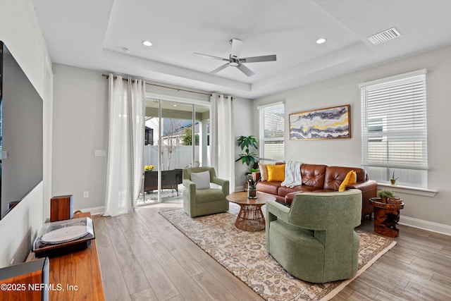 living room with hardwood / wood-style floors, ceiling fan, and a tray ceiling