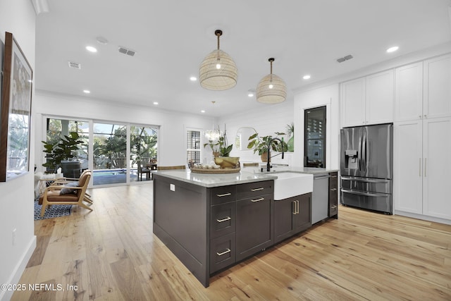 kitchen featuring light hardwood / wood-style floors, appliances with stainless steel finishes, a kitchen island with sink, hanging light fixtures, and white cabinets