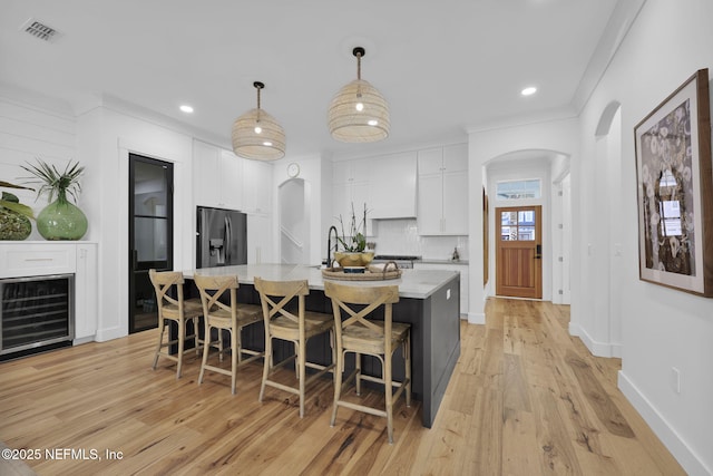 kitchen featuring pendant lighting, beverage cooler, white cabinetry, an island with sink, and stainless steel fridge with ice dispenser