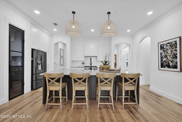 kitchen with a kitchen island with sink, white cabinets, stainless steel refrigerator with ice dispenser, and hanging light fixtures