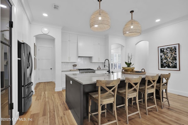 kitchen with white cabinetry, decorative backsplash, sink, hanging light fixtures, and a center island with sink