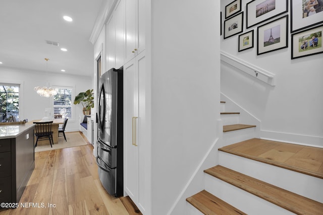 interior space with black refrigerator, light wood-type flooring, a chandelier, pendant lighting, and white cabinets