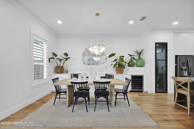 dining room featuring crown molding, a chandelier, wine cooler, and light hardwood / wood-style floors