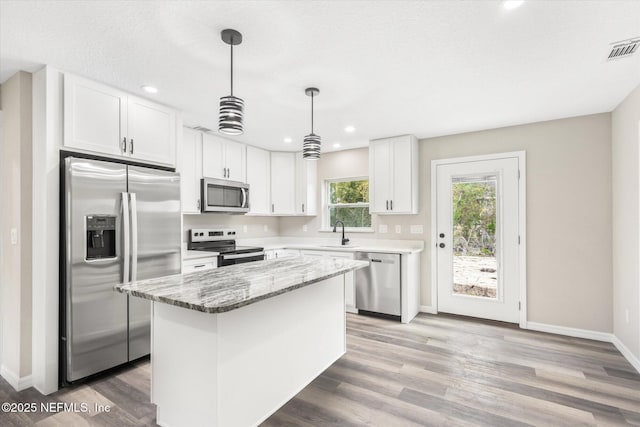 kitchen with appliances with stainless steel finishes, a kitchen island, decorative light fixtures, white cabinetry, and stone countertops