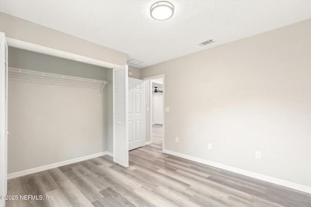 unfurnished bedroom with a textured ceiling, a closet, and light wood-type flooring