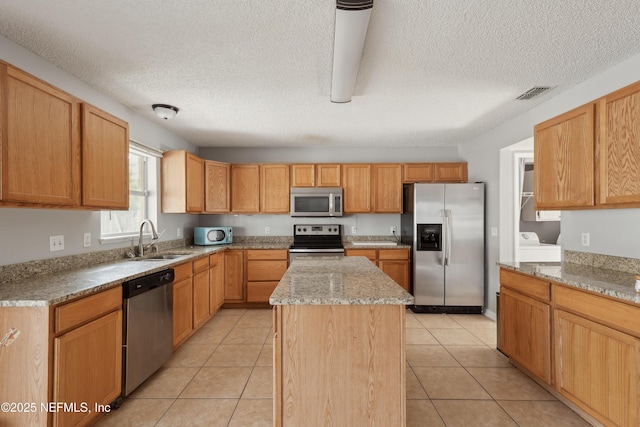 kitchen featuring sink, light stone counters, light tile patterned flooring, a center island, and stainless steel appliances