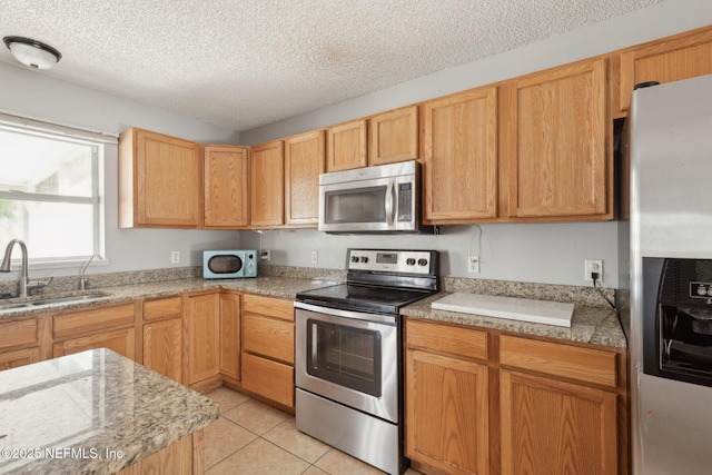 kitchen featuring a textured ceiling, stainless steel appliances, sink, light stone counters, and light tile patterned floors