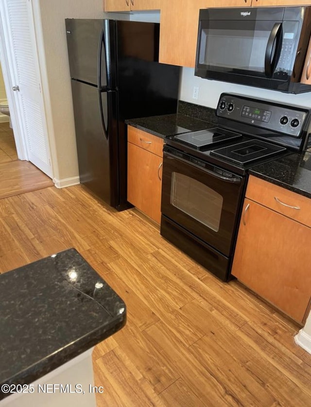 kitchen featuring black appliances, dark stone counters, and light hardwood / wood-style floors