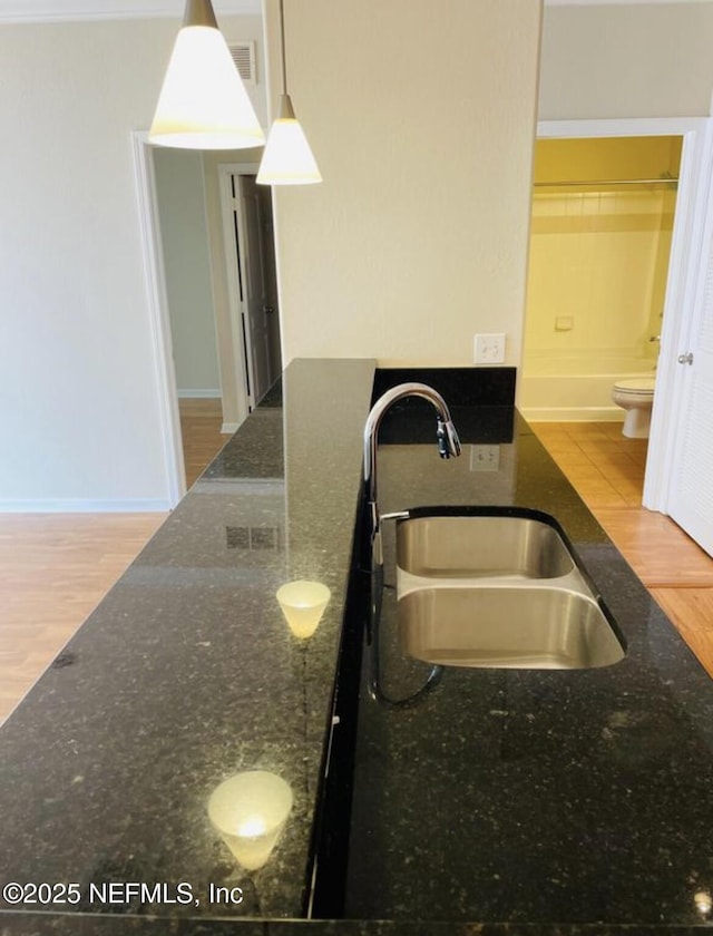 kitchen with pendant lighting, light hardwood / wood-style floors, dark stone counters, and sink