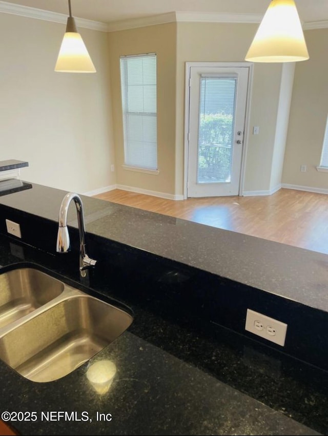 kitchen featuring dark stone countertops, hardwood / wood-style floors, pendant lighting, sink, and ornamental molding