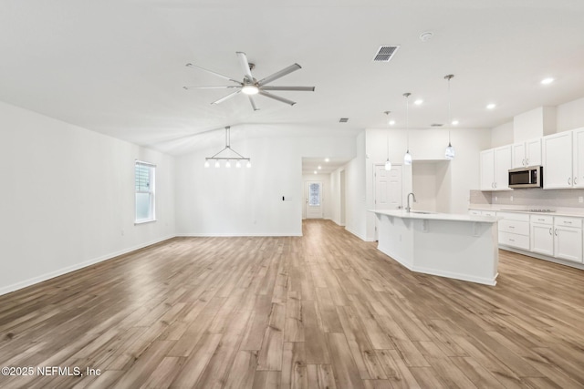 kitchen featuring pendant lighting, light hardwood / wood-style floors, an island with sink, and white cabinets