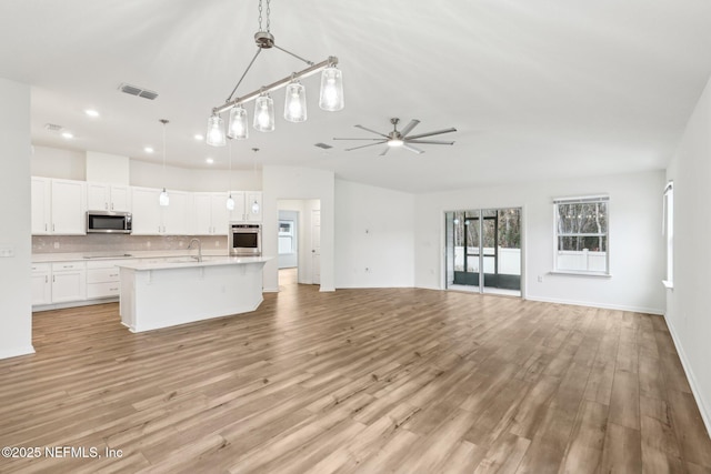 kitchen featuring appliances with stainless steel finishes, hanging light fixtures, white cabinets, a center island with sink, and decorative backsplash