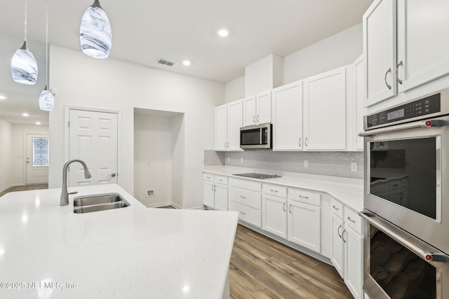 kitchen with white cabinetry, sink, hanging light fixtures, and appliances with stainless steel finishes