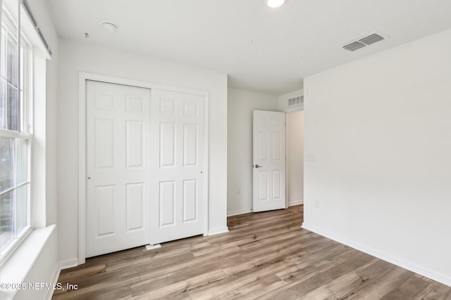 unfurnished bedroom featuring multiple windows, light hardwood / wood-style floors, and a closet