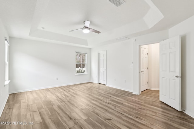 unfurnished room with ceiling fan, a tray ceiling, and light hardwood / wood-style floors