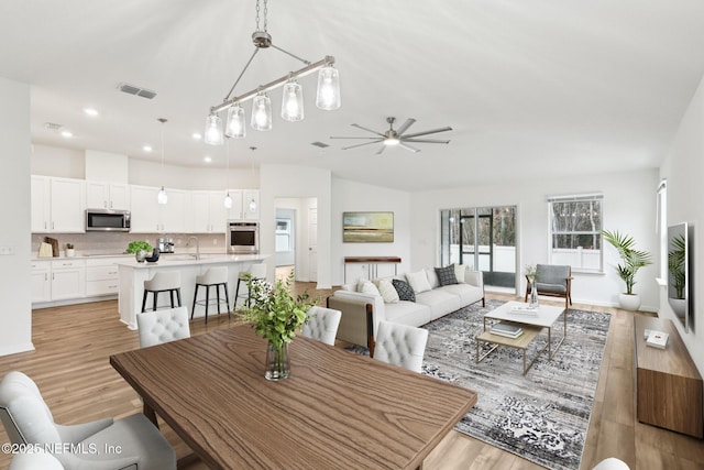 dining space with ceiling fan, lofted ceiling, sink, and light hardwood / wood-style floors