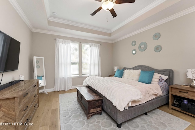 bedroom with ceiling fan, crown molding, a tray ceiling, and light hardwood / wood-style flooring