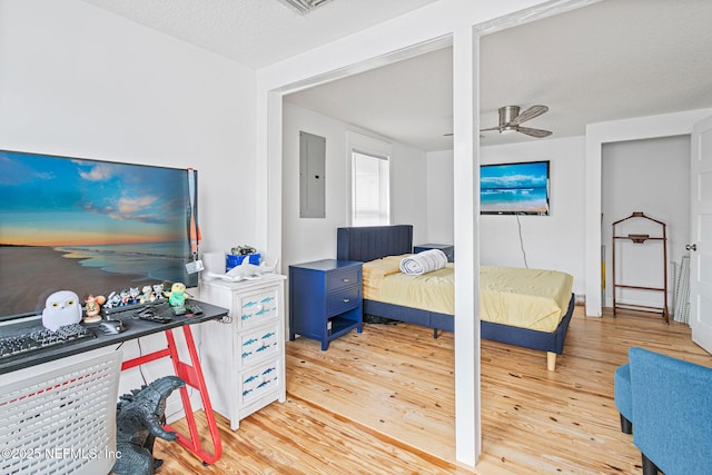 bedroom with ceiling fan, light wood-type flooring, a textured ceiling, and electric panel