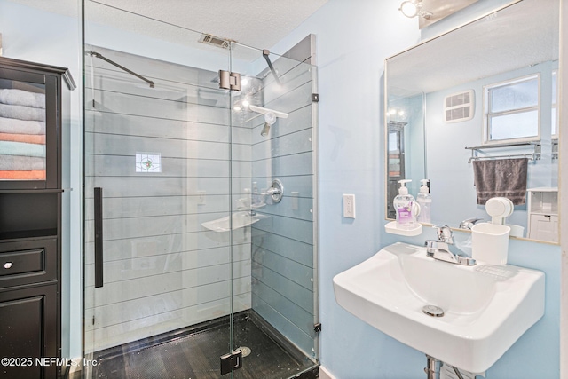 bathroom with a shower with shower door, sink, and a textured ceiling