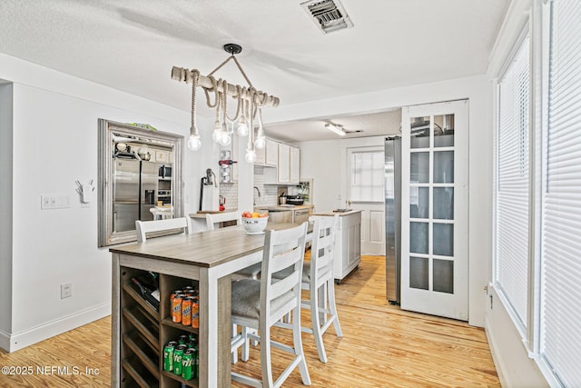 kitchen featuring a notable chandelier, pendant lighting, light hardwood / wood-style flooring, stainless steel fridge with ice dispenser, and white cabinets