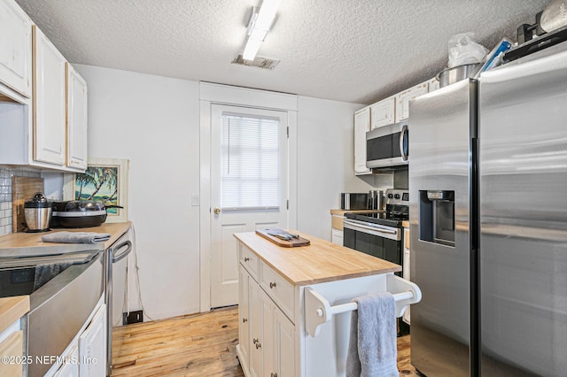 kitchen featuring a textured ceiling, white cabinets, a center island, wood counters, and stainless steel appliances