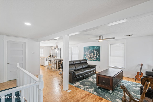 living room with ceiling fan with notable chandelier, a textured ceiling, and light wood-type flooring