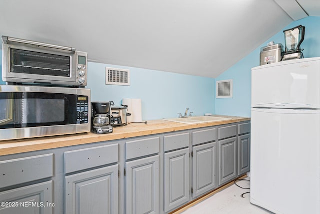 kitchen featuring white fridge, wooden counters, gray cabinets, lofted ceiling, and sink