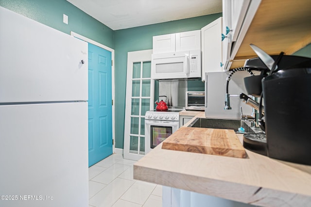 kitchen with light tile patterned floors, white cabinetry, sink, and white appliances