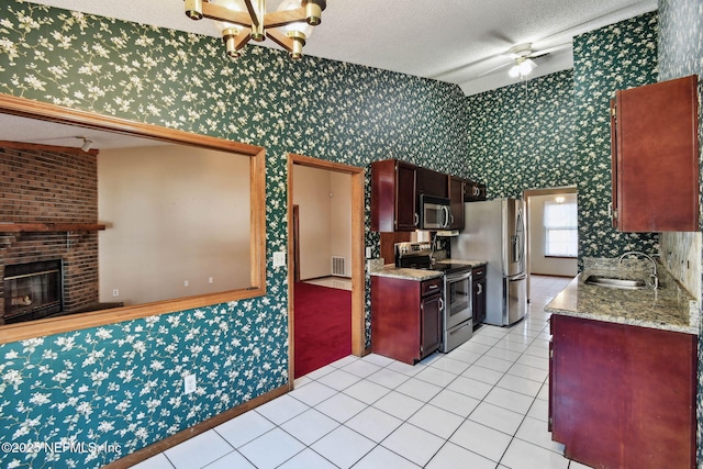 kitchen featuring a brick fireplace, appliances with stainless steel finishes, light tile patterned flooring, a textured ceiling, and sink