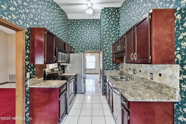 kitchen featuring light tile patterned floors, ceiling fan, appliances with stainless steel finishes, light stone counters, and sink