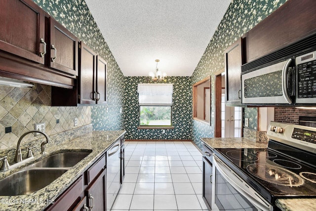 kitchen featuring an inviting chandelier, stainless steel appliances, hanging light fixtures, light stone countertops, and sink