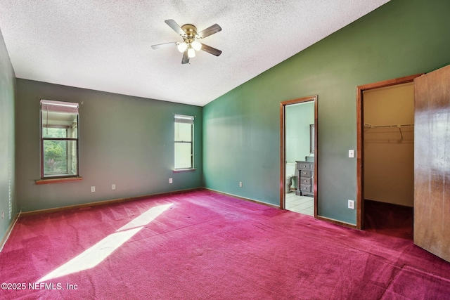 unfurnished bedroom with ceiling fan, a closet, vaulted ceiling, a walk in closet, and multiple windows