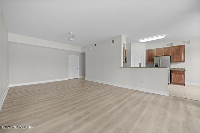 unfurnished living room featuring ceiling fan, sink, and light wood-type flooring