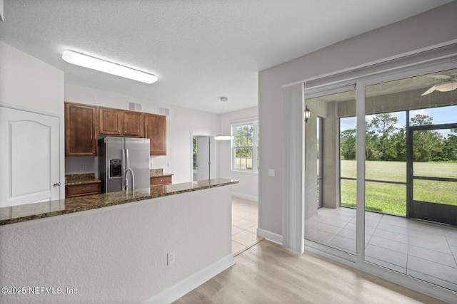 kitchen with a textured ceiling, dark stone counters, sink, stainless steel fridge with ice dispenser, and light wood-type flooring