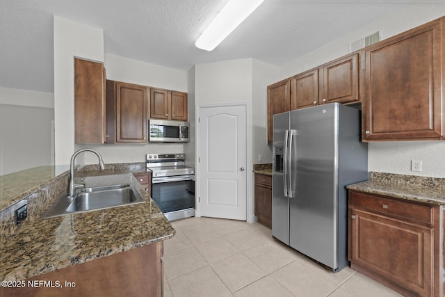 kitchen with a textured ceiling, stainless steel appliances, dark stone counters, sink, and light tile patterned flooring