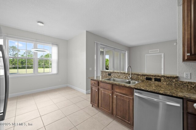 kitchen with light tile patterned floors, dark stone countertops, dishwasher, a textured ceiling, and sink