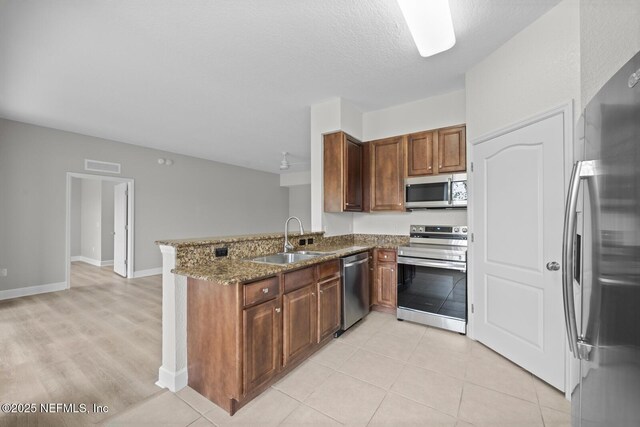 kitchen featuring kitchen peninsula, stainless steel appliances, light tile patterned flooring, dark stone countertops, and sink