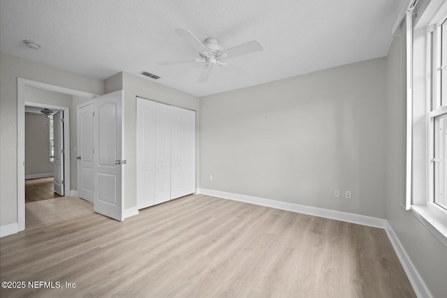 unfurnished bedroom featuring light wood-type flooring, ceiling fan, a closet, and multiple windows