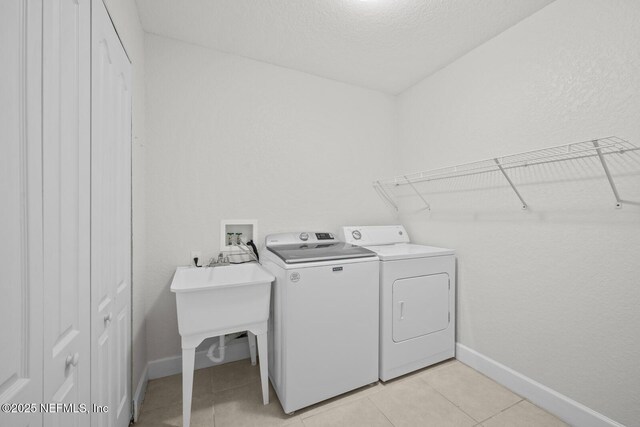 laundry area with light tile patterned floors, washing machine and clothes dryer, and a textured ceiling