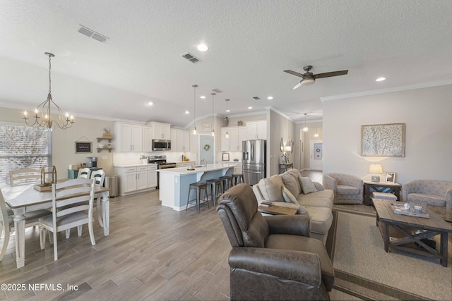 living room featuring ceiling fan with notable chandelier, a textured ceiling, sink, light wood-type flooring, and crown molding