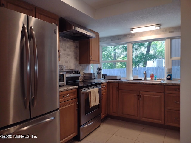 kitchen featuring light stone countertops, appliances with stainless steel finishes, wall chimney exhaust hood, sink, and light tile patterned floors