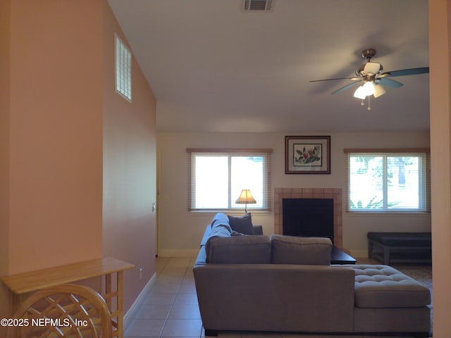 living room with ceiling fan, light tile patterned floors, a tiled fireplace, and plenty of natural light