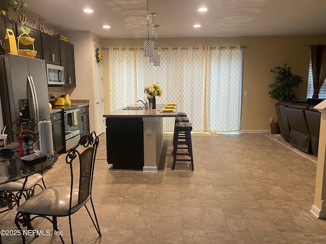 kitchen with pendant lighting, a center island with sink, a breakfast bar, stainless steel appliances, and light stone counters