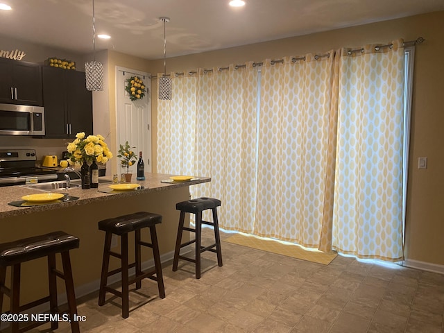 kitchen with appliances with stainless steel finishes, decorative light fixtures, sink, stone countertops, and a breakfast bar