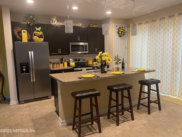 kitchen featuring a breakfast bar area, appliances with stainless steel finishes, hanging light fixtures, and an island with sink